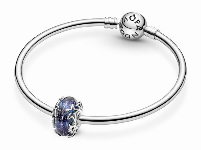 Ein filigraner Pandora Charm mit der Bezeichnung Galaxie Blau und Stern aus Murano-Glas, umgeben von einem Sterling Silber Armband mit funkelnden Kristallen in Blau.