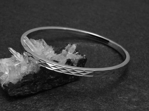 Silber Armreifen funkeln in rhodiniertem Finish, 4 mm breit, 18 cm lang, elegant auf einem schwarzen Untergrund mit Kristallen drapiert. Hersteller Juwelier Harnisch.