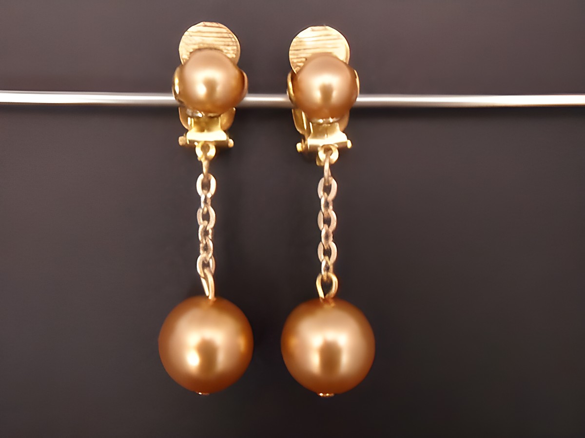 Glänzende goldfarbene Ohrclips mit einem zeitlosen Design aus Kunstharz, verbunden durch eine feine Kette, die edel und elegant wirkt, Hersteller Juwelier Harnisch.