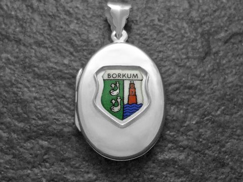 Silbernes Medaillon mit dem Inselwappen von Borkum, das eine grüne und blaue Farbgebung zeigt, mit stilisierten Meerestieren und einem Leuchtturm. Hersteller ist Juwelier Harnisch.
