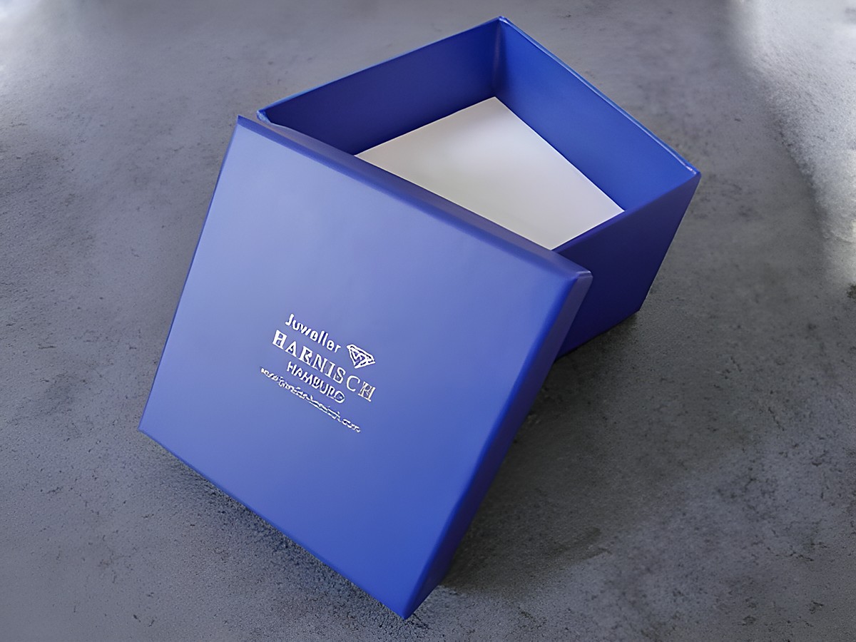 Eine viereckige, blaue Geschenkbox mit einem weißen Innenraum, 85 x 85 x 60 mm, mit dem Logo von Juwelier Harnisch auf der Oberseite. Ideal für hochwertige Geschenke.