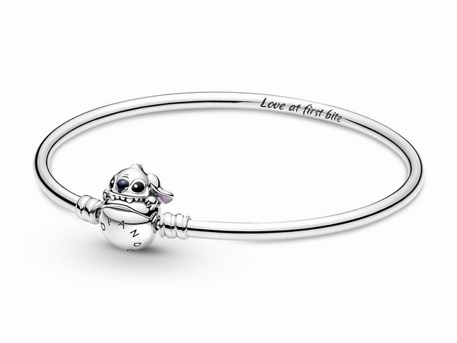 591683017-0 Ein eleganter Armreif aus Sterling Silber mit einem bunten, lächelnden Stitch-Anhänger von Disney, versehen mit dem Schriftzug Love at first bite und der Marke Pandora.