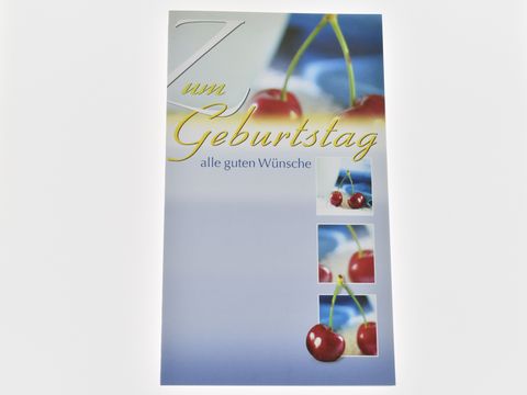 Eine Geburtstagskarte mit Kirschenmotiven, auf der steht "Zum Geburtstag" und "alle guten Wünsche". Die Farben sind überwiegend blau und rot, was eine fröhliche Stimmung vermittelt. Hersteller: Juwelier Harnisch.
