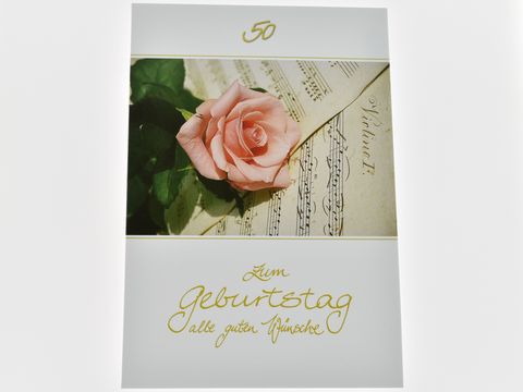 Geburtstagskarte mit einer rosafarbenen Rose auf Notenpapier, verziert mit der Aufschrift Zum Geburtstag. Hersteller Juwelier Harnisch.