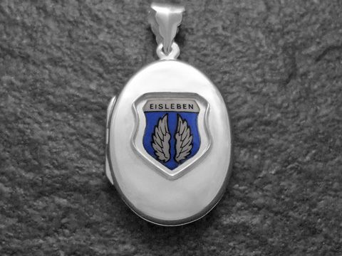 Das Bild zeigt ein silbernes Medaillon mit dem Stadtwappen von Eisleben. Das Wappen ist mit blauen und weißen Elementen gestaltet und hebt die Flügel hervor. Hersteller ist Juwelier Harnisch aus Sachsen-Anhalt.