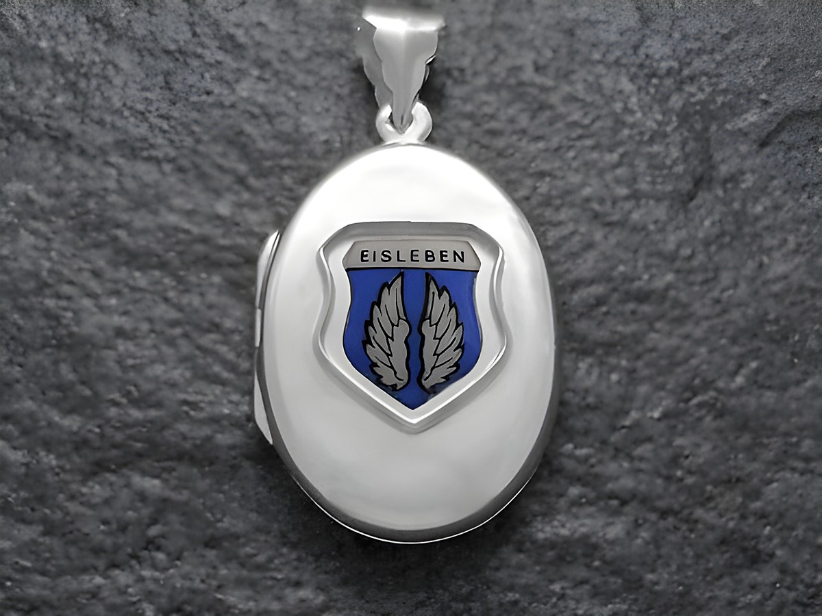 Das Bild zeigt ein silbernes Medaillon mit dem Stadtwappen von Eisleben. Das Wappen ist mit blauen und weißen Elementen gestaltet und hebt die Flügel hervor. Hersteller ist Juwelier Harnisch aus Sachsen-Anhalt.