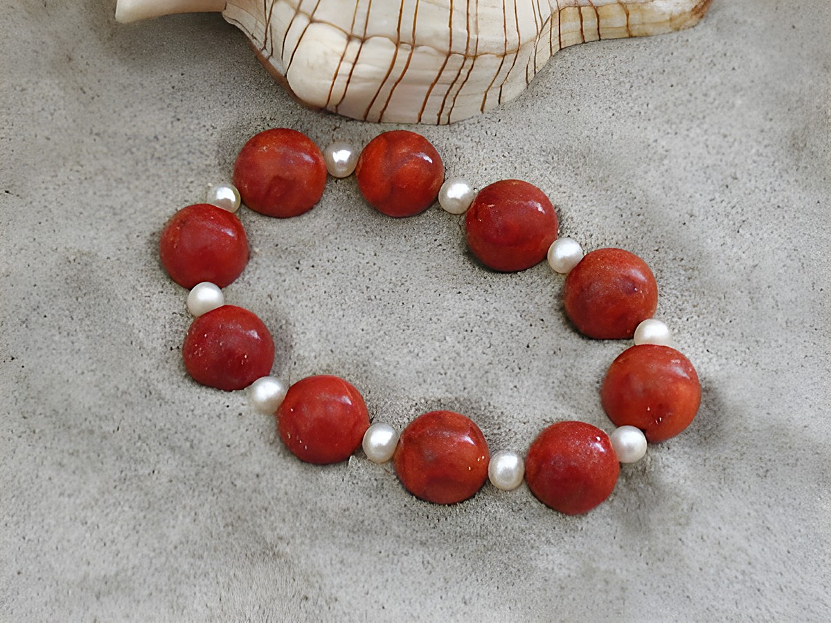 Korallenschmuck Armband 20 cm Gummizug mit Zuchtperlen in rot und weiß, hergestellt von Juwelier Harnisch, schön auf sandigem Hintergrund präsentiert.