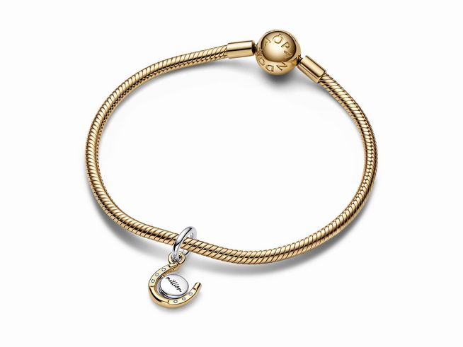 Die Pandora 762713C01 Bicolor Drehende Hufeisen-Scheibe Charm-Anhänger aus Sterling Silber und gelbgoldener Vergoldung mit Zirkonia ist an einem klassischen Armband befestigt.