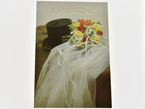 Hochzeitskarte mit Zylinder, Schleier und Brautstrauß in sanften Farben, hergestellt von Juwelier Harnisch. Der Schriftzug zur Verlobung ist elegant platziert.