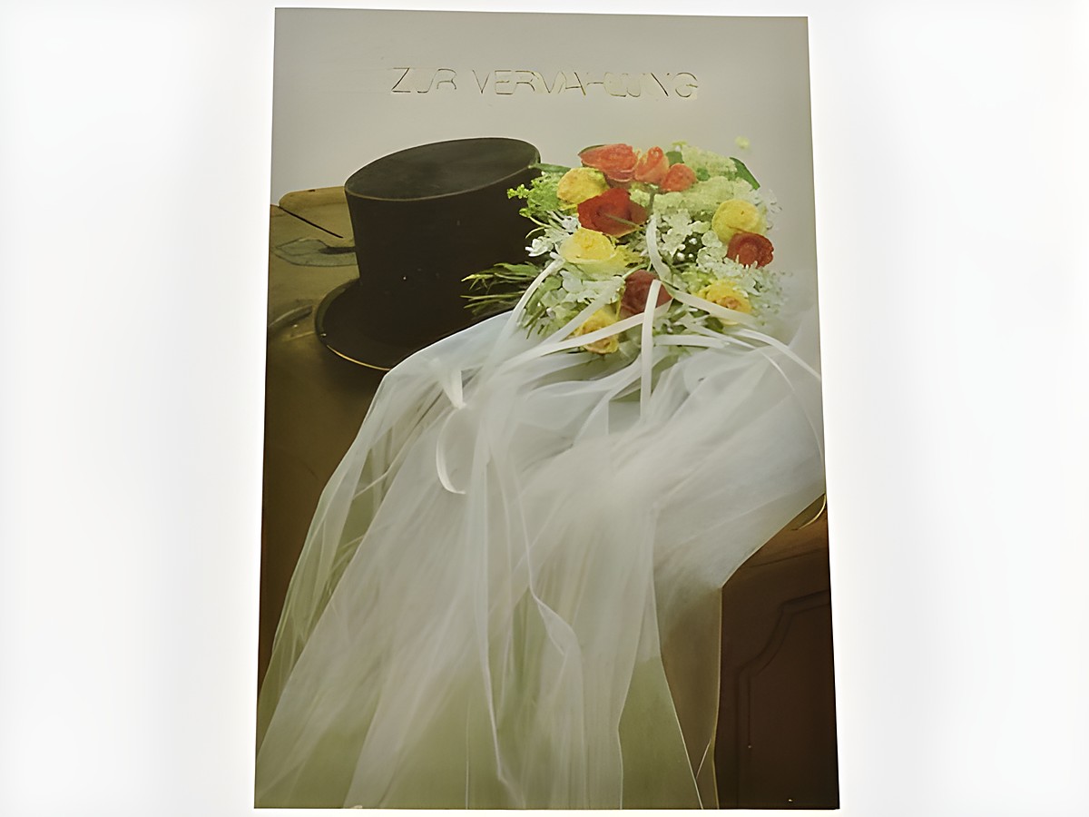 Hochzeitskarte mit Zylinder, Schleier und Brautstrauß in sanften Farben, hergestellt von Juwelier Harnisch. Der Schriftzug zur Verlobung ist elegant platziert.