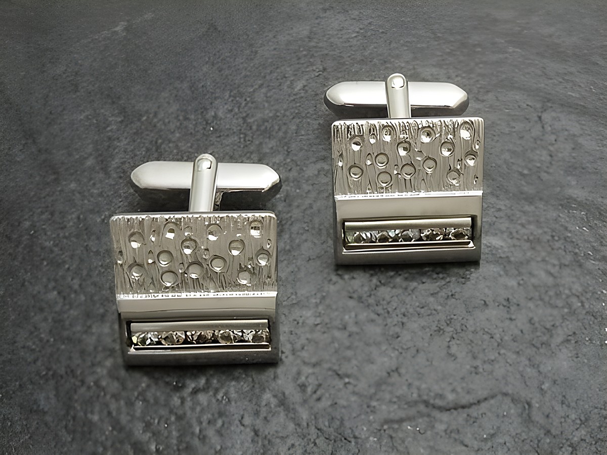 Manschettenknöpfe in silberfarben mit weißen Strass Steinen, Hersteller Juwelier Harnisch, modernes Design mit glänzender Oberfläche und dekorativem Strassband. Ideal für elegante Anlässe.