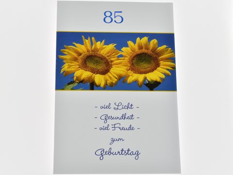 Geburtstagskarte mit zwei Sonnblumen auf blauem Hintergrund, in der oberen Ecke die Zahl 85, darunter der Schriftzug viel Licht, Gesundheit, viel Freude zum Geburtstag. Hersteller Juwelier Harnisch.