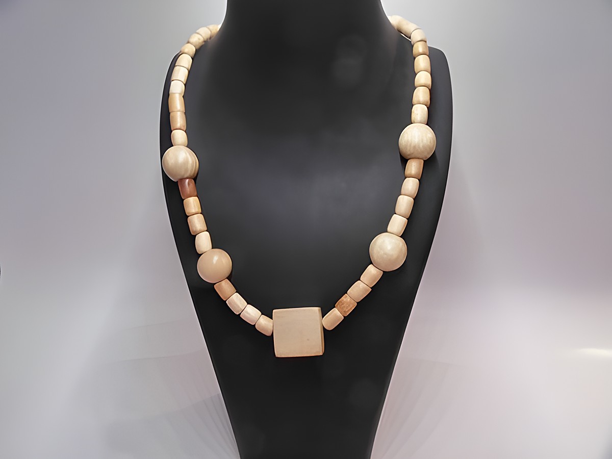 Eine naturbraune Holzkette von Juwelier Harnisch mit einer Länge von 60 cm. Die Kette besteht aus verschiedenen Holzperlen mit einem quadratischen Element in der Mitte.