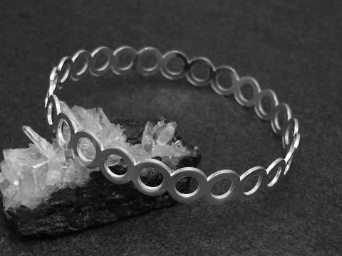 Silber Armreifen mit Kreisen, 9,3 mm breit und 20 cm lang, hergestellt von Juwelier Harnisch, auf schwarzem Untergrund und dekoriert mit kristallähnlichen Steinen.