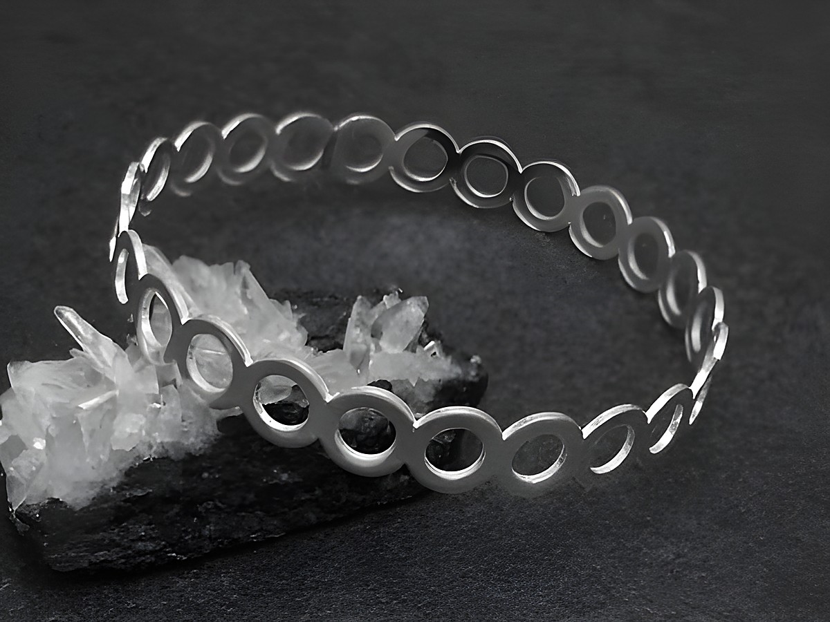 Silber Armreifen mit Kreisen, 9,3 mm breit und 20 cm lang, hergestellt von Juwelier Harnisch, auf schwarzem Untergrund und dekoriert mit kristallähnlichen Steinen.