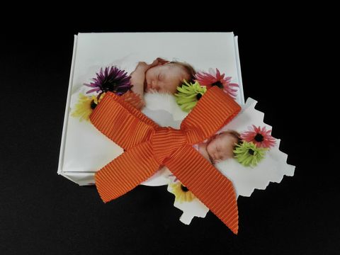 100182-0 Geschenkschachtel für die Taufe oder Geburt eines Babys mit einem dekorativen Motiv von schlafenden Säuglingen, verziert mit bunten Blumen und einer orangefarbenen Schleife, Hersteller Juwelier Harnisch, Maße 60 mm.