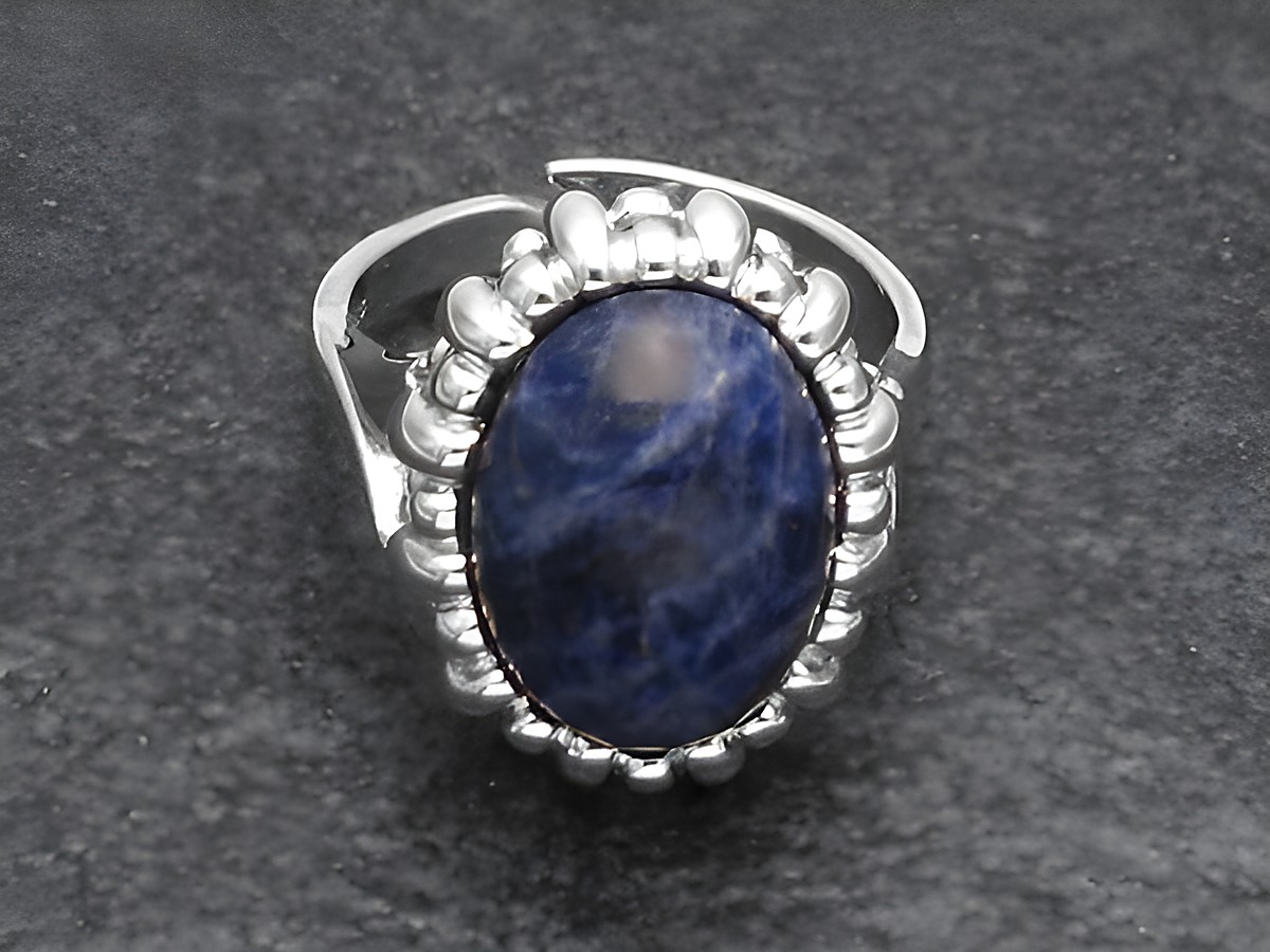 Silberring mit verstellbarem Design, besetzt mit einem ovalen Sodalithstein, umgeben von einem geschwungenen, rhodinierten Rahmen, elegant und einzigartig.