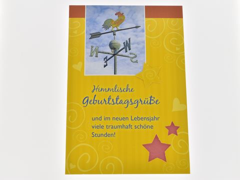 Eine gelbe Geburtstagskarte mit einem Wetterhahn auf der Vorderseite, verziert mit bunten Sternen und dem Text himmlische Geburtstagsgrüße sowie einem freundlichen Wunsch für viele schöne Stunden. Hersteller Juwelier Harnisch.