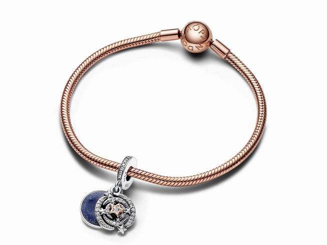 Silberner Charm-Anhänger in Form einer Doppelsternschnuppe, verziert mit Zirkonia in Blau und Roségold, an einem zarten Armband von Pandora.