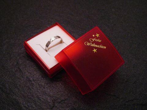 Eine rote Geschenkschachtel mit der Aufschrift Frohe Weihnachten öffnet sich und zeigt einen silbernen Ring im Innenraum, Hersteller Juwelier Harnisch, Größe 4,5 cm, ideal für Weihnachten.