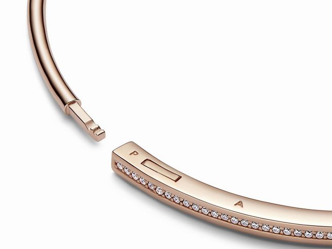 Eleganter Pandora Armreif aus roségoldvergoldetem Metall, verziert mit klaren Zirkonia, leicht gebogen mit öffnendem Verschluss und dezentem Logo, ideal für femininen Schmuckstil.