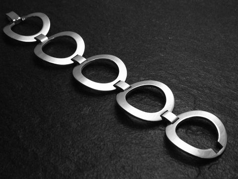 Silberarmband futuristisch 18 cm Design von Juwelier Harnisch ohne Stein, besteht aus mehreren eleganten und geschwungenen Elementen, präsentiert auf einem dunklen Untergrund.