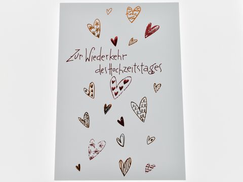 Weiße Hochzeitskarte mit roten Herzchen, verziert mit verschiedenen Herzmotiven und dem Text zur Wiederkehr des Hochzeitstages, Hersteller Juwelier Harnisch.