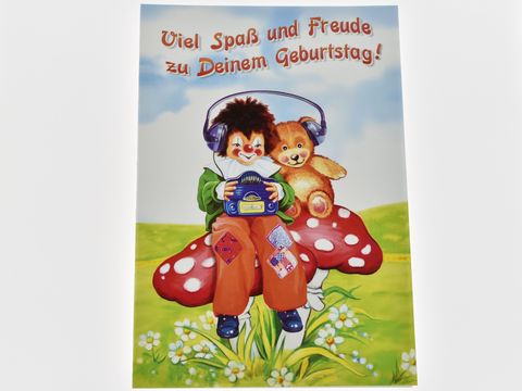 Eine Geburtstagskarte mit einem Clown, der einen Teddy umarmt, sitzt auf einem roten Glückspilz. Im Hintergrund stehen Blumen und der Text Viel Spaß und Freude zu Deinem Geburtstag.