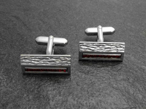 10073-0 Silberfarbene Manschettenknöpfe mit roten Strasssteinen von Juwelier Harnisch, elegantes Design mit strukturiertem Oberflächenfinish und glatten Akzenten, ideal für festliche Anlässe.