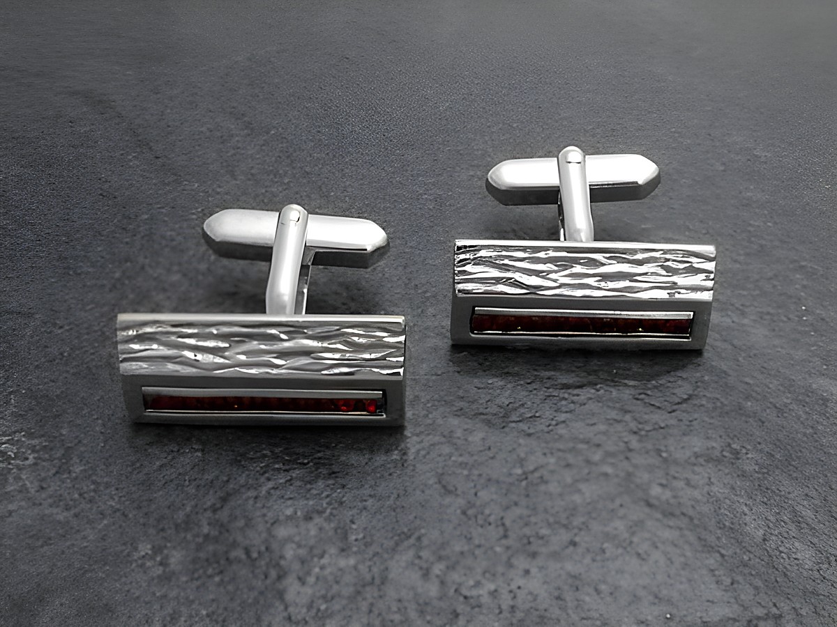 Silberfarbene Manschettenknöpfe mit roten Strasssteinen von Juwelier Harnisch, elegantes Design mit strukturiertem Oberflächenfinish und glatten Akzenten, ideal für festliche Anlässe.