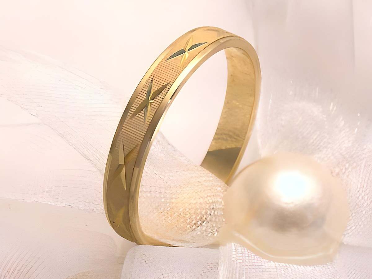 Trauring Ehering CROSS aus Gold 333 in Größe 56/17,8, verziert mit feinen Mustern, elegant auf einem schlichten Untergrund drapiert neben einer Perle. Hersteller Juwelier Harnisch.