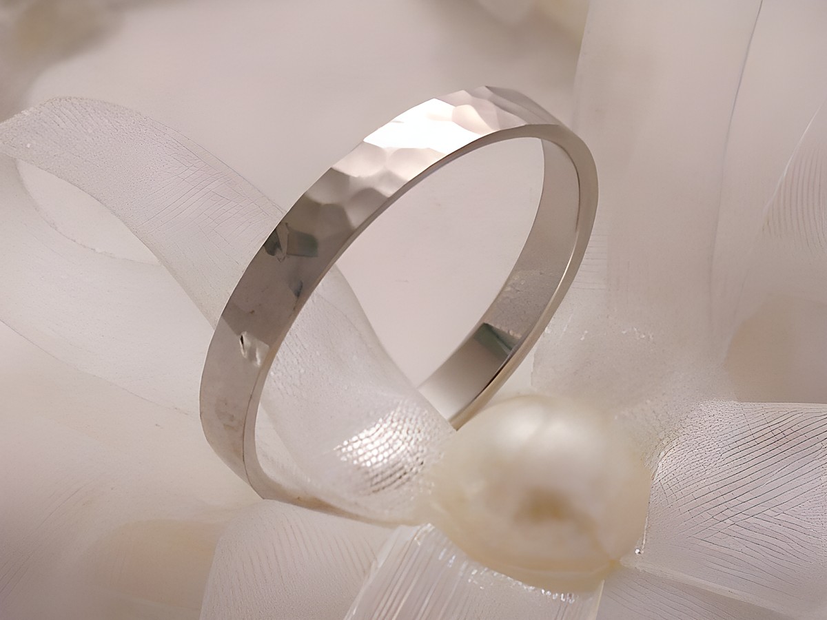 Trauring Ehering aus Weißgold 333 in Größe 64/20,4 mit einer gehämmerten Oberfläche, elegant präsentiert auf einem dekorativen weißen Stoff mit Perle. Hersteller: Juwelier Harnisch.
