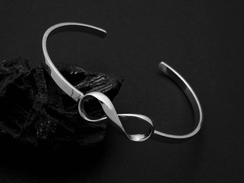 Silber Armreifen Unendlich 18 cm symbolisch Hersteller Juwelier Harnisch Armreifen elegant auf schwarzem Hintergrund mit geschwungener Unendlichkeitsschleife.