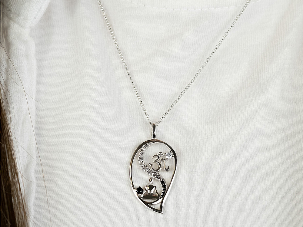 Kette aus Silber mit Tropfenanhänger in Yin Yang Form, verziert mit Zirkonia, Länge 42 cm, erweiterbar um 4 cm, auf einem weißen Oberteil getragen.