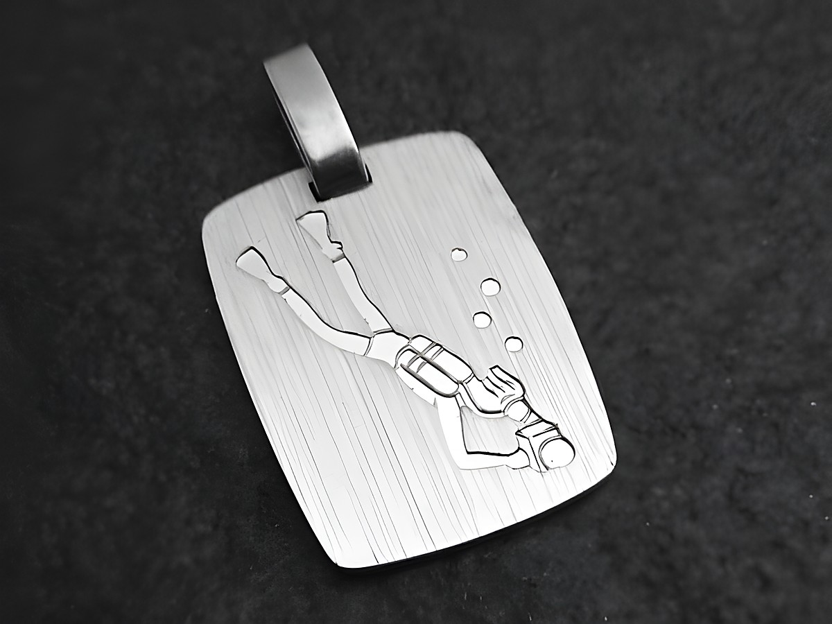 Silber Anhänger mit einer Gravur eines Tauchers, der unter Wasser schwimmt. Der Anhänger hat eine rechteckige Form und zeigt Blasen, die um den Taucher herum aufsteigen.