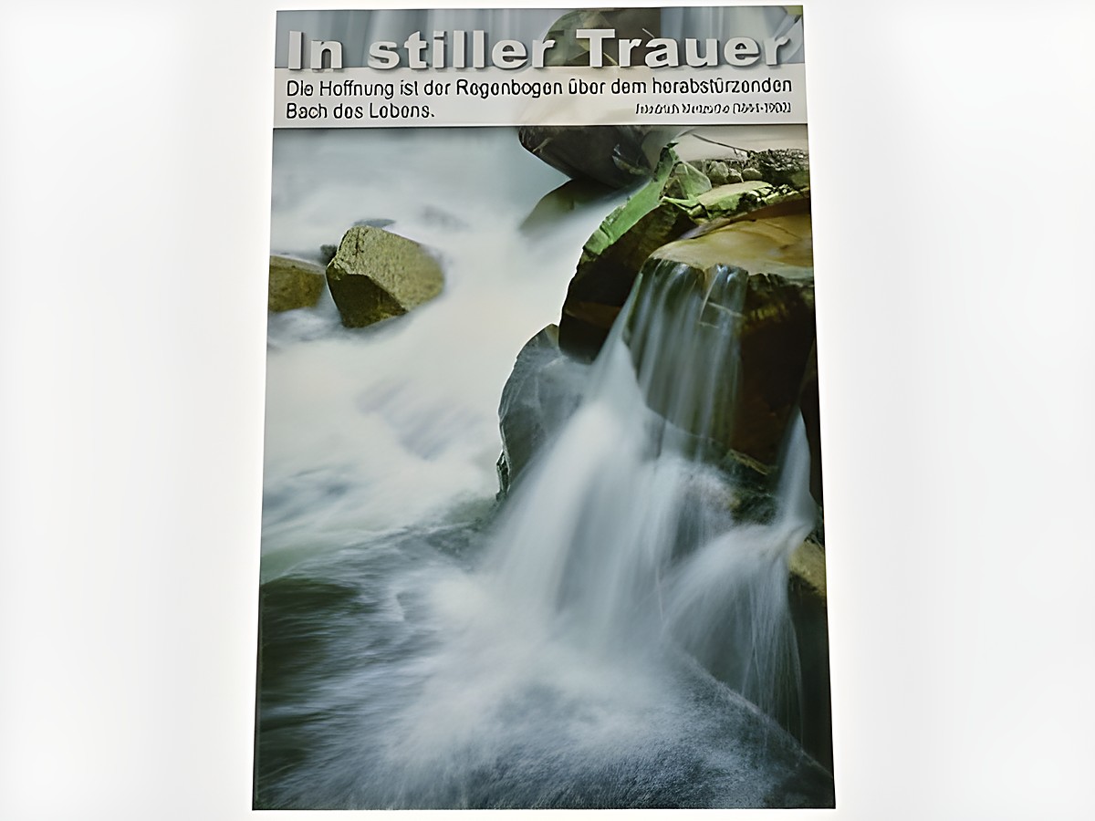 Trauerkarte mit einem sanften Wasserfall, umgeben von Steinen. Oben der Schriftzug In stiller Trauer und ein Zitat von Friedrich Nietzsche. Hersteller Juwelier Harnisch.