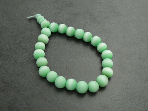 Powerarmband mit Gummizug in hellgrün mit 14 cm Glassteinen, Hersteller Juwelier Harnisch, zeigt eine durchgehende Reihe von mattierten, runden Perlen.