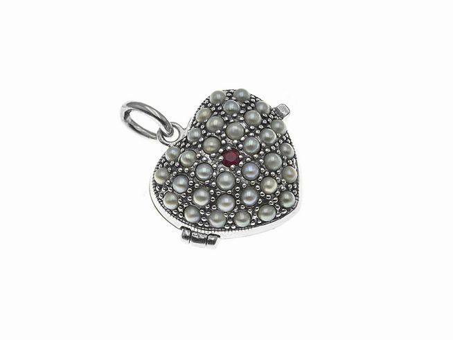 Ein zeitloses silbernes Medaillon in Herzform, geschmückt mit weißen Perlen und einem rubinrot schimmernden Stein, gefertigt von Juwelier Harnisch.