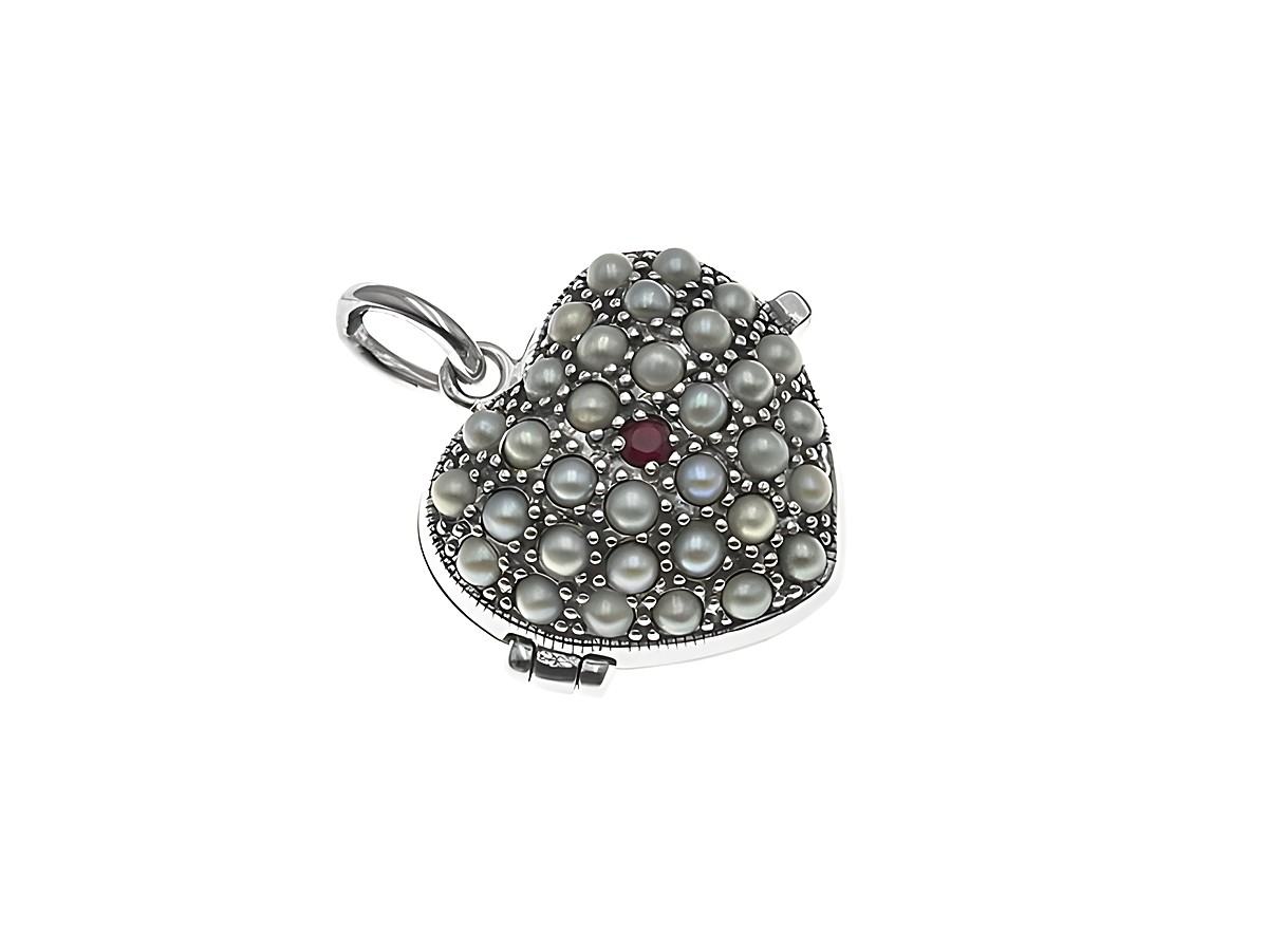 Ein zeitloses silbernes Medaillon in Herzform, geschmückt mit weißen Perlen und einem rubinrot schimmernden Stein, gefertigt von Juwelier Harnisch.