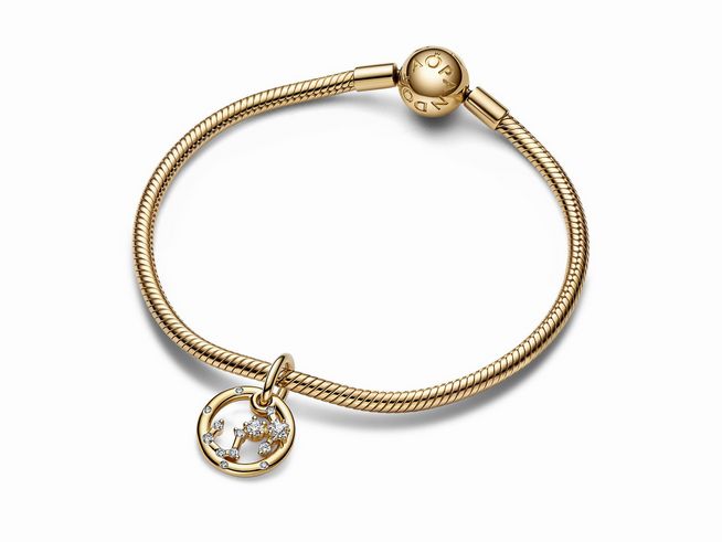 Charm-Anhänger von Pandora mit dem Sternzeichen Skorpion, gefertigt aus gelbgold vergoldetem Material und besetzt mit Zirkonia, hängt an einem feinen Armband.