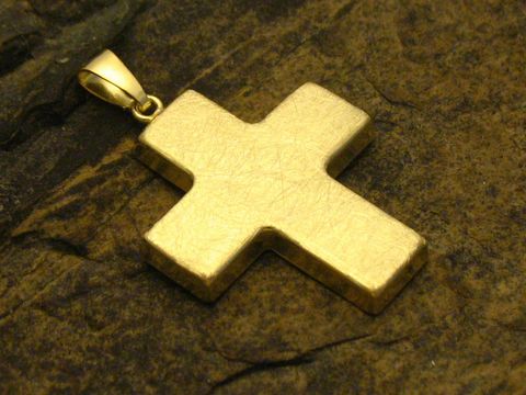Kreuz aus Gold 333, Anhänger in klassischem Design, hergestellt von Juwelier Harnisch, auf rauem Untergrund platziert, mit glatter und glänzender Oberfläche.