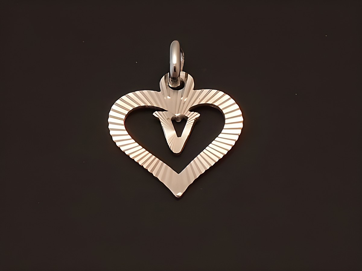 Ein herzförmiger Anhänger aus rhodiniertem Sterling Silber mit dem Buchstaben V, verziert mit feinen Rillen und einer Öse zum Einhängen, hergestellt von Juwelier Harnisch.