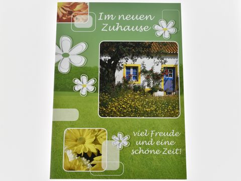 Eine Grußkarte mit dem Text Im neuen Zuhause, geschmückt mit Blumen, einer idyllischen Hausansicht und einem verdeckten Baum, ideal für Glückwünsche von Juwelier Harnisch.
