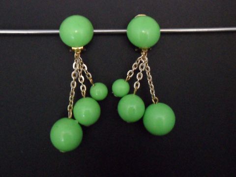 Ohrclip in grasgrün zeitlos mit goldfarbenen Akzenten und Kunstharz, designet von Juwelier Harnisch, zeigt elegante Ketten mit verschieden großen Perlen für einen auffälligen Look.