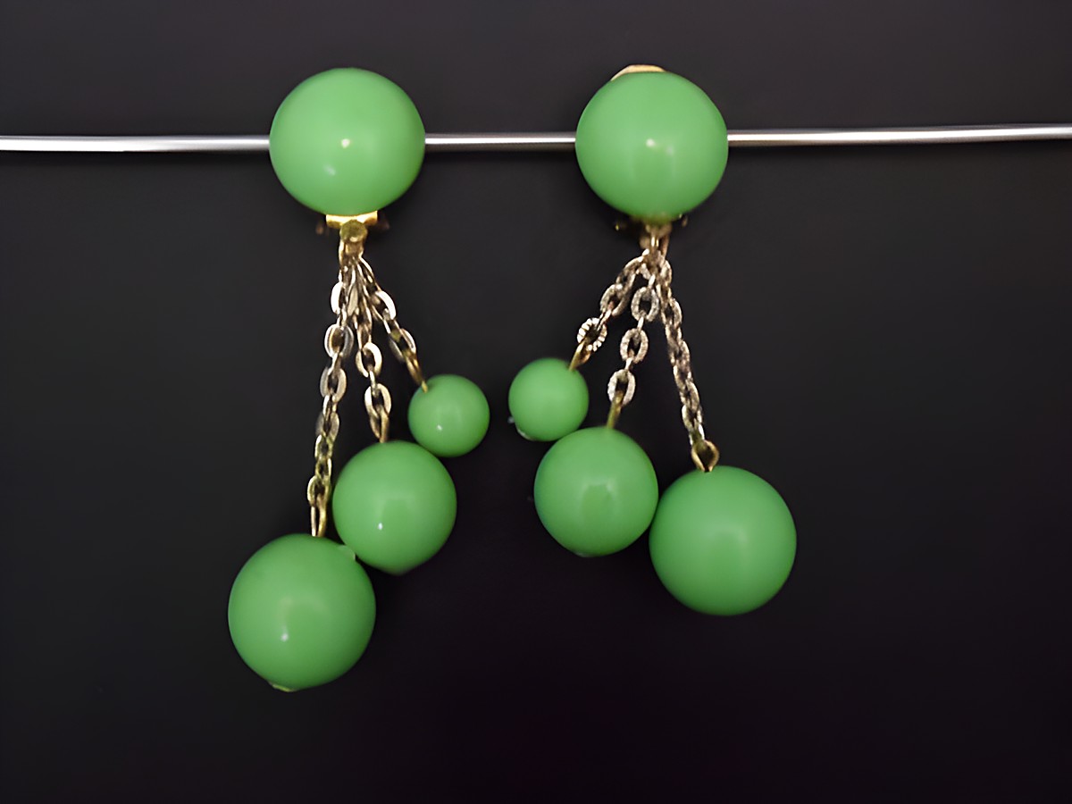 Ohrclip in grasgrün zeitlos mit goldfarbenen Akzenten und Kunstharz, designet von Juwelier Harnisch, zeigt elegante Ketten mit verschieden großen Perlen für einen auffälligen Look.