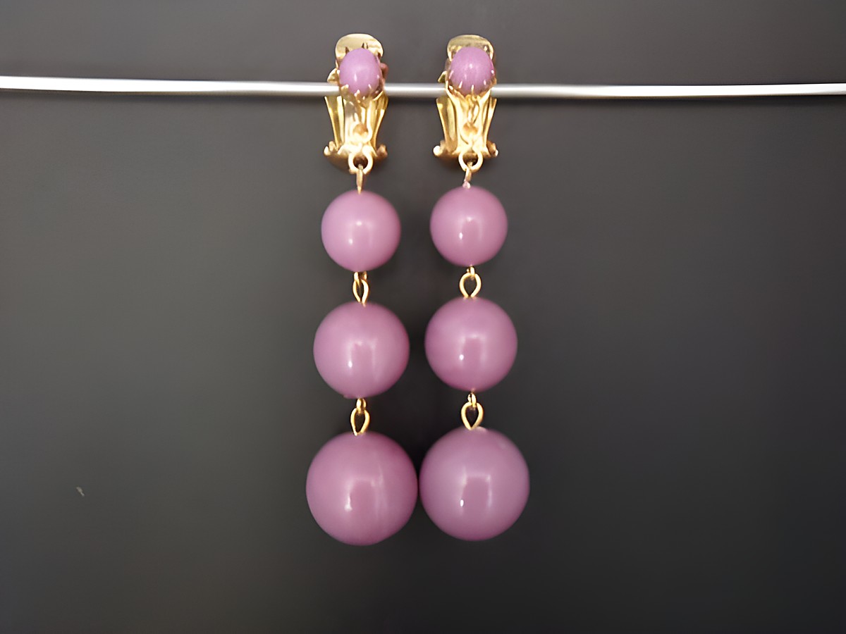 Violette Ohrclips aus Kunstharz mit goldfarbenen Akzenten, gefertigt von Juwelier Harnisch. Zeitloses Design mit zwei hängenden Kugeln in verschiedenen Größen. Ideal für elegante Anlässe.