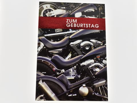 Eine Geburtstagskarte mit dem Schriftzug Zum Geburtstag, die Motorräder zeigt, im Hintergrund sind glänzende Chromteile und schwarze Motorraddetails zu erkennen, hergestellt von Juwelier Harnisch.