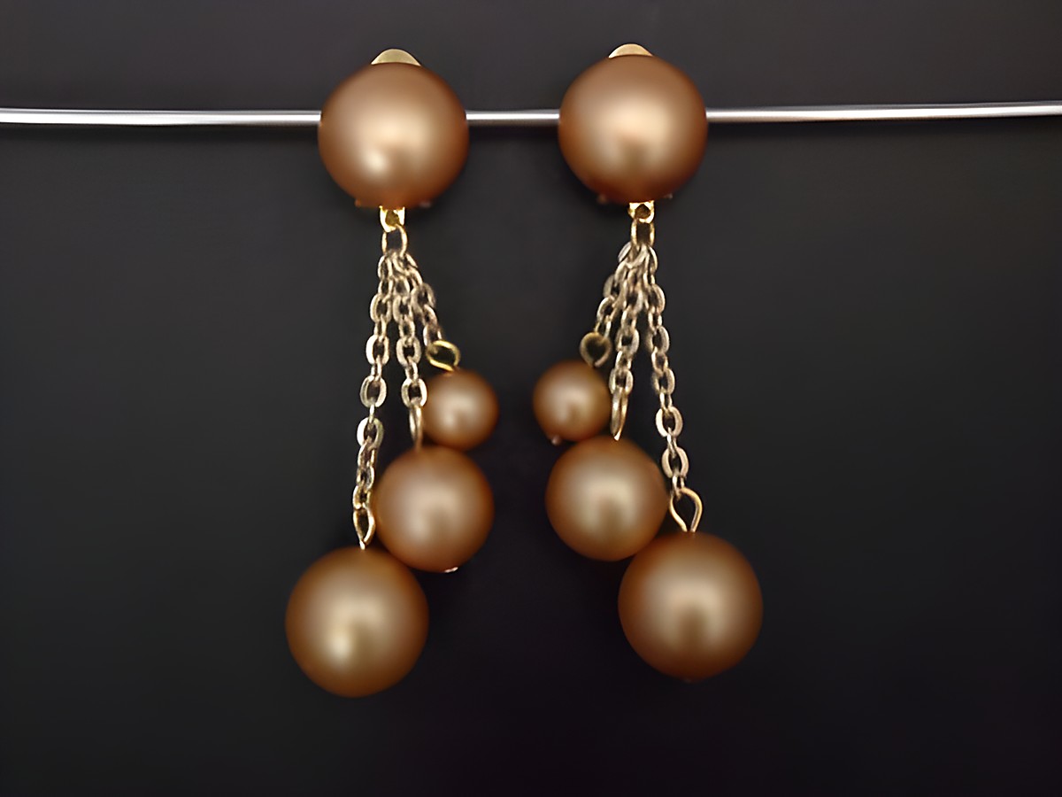 Beige zeitlose Ohrclips aus Kunstharz mit goldfarbenen Kettenanhängern in schimmerndem seidenmattem Finish, Hersteller Juwelier Harnisch, elegant und verspielt zugleich.