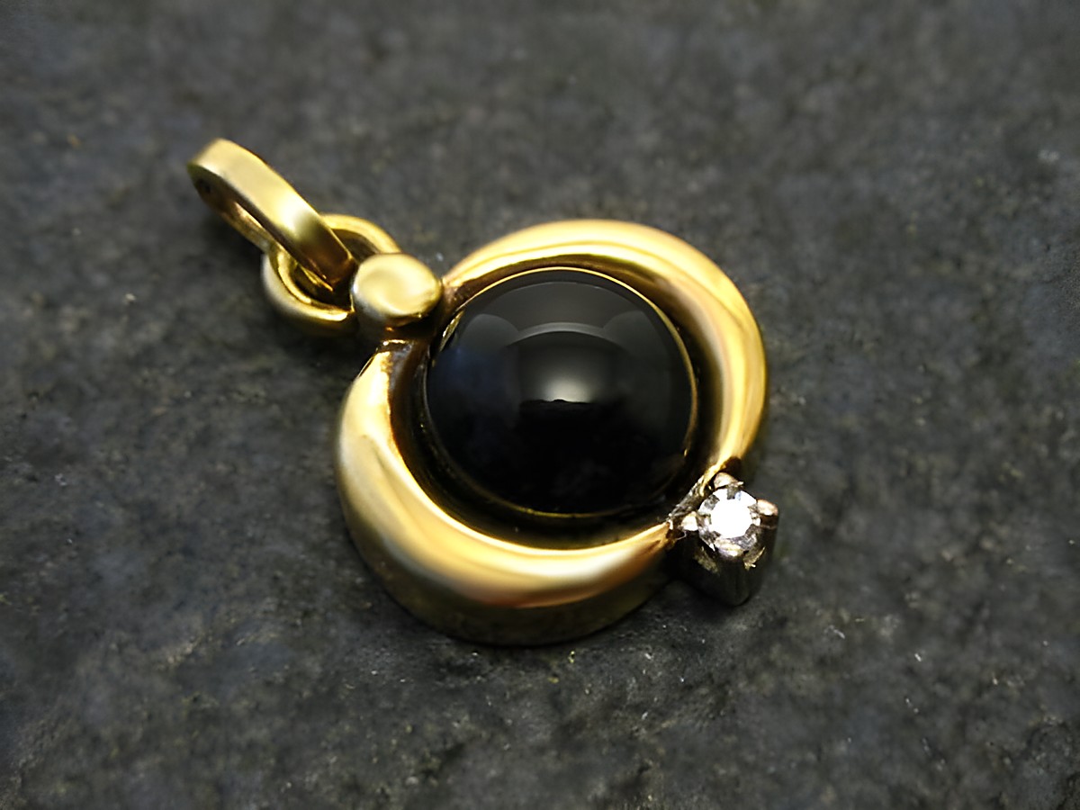 Onyx mit Diamant - Gold Anhänger in runder Form, zentraler schwarzer Onyxstein, umgeben von glänzendem Gold und einem funkelnden Diamanten, Hersteller Juwelier Harnisch.