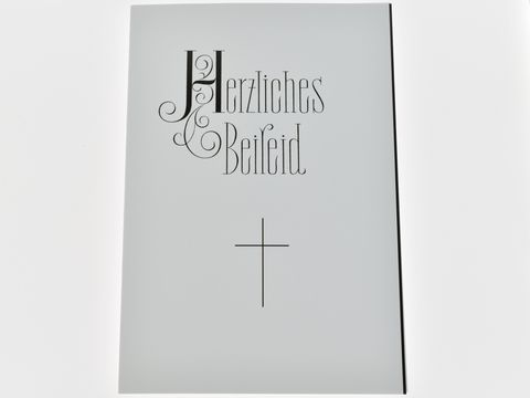 Trauerkarte mit dem Aufdruck Herzliches Beileid in eleganter Schrift und einem Kreuz darunter, hergestellt von Juwelier Harnisch.